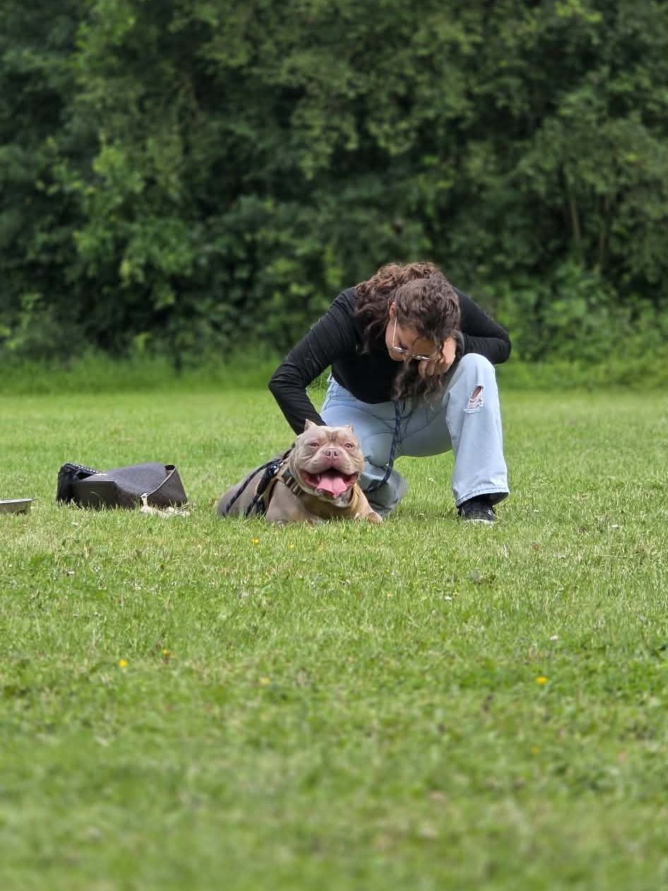 Précila accroupie dans l'herbe, la main posée sur un chien souriant